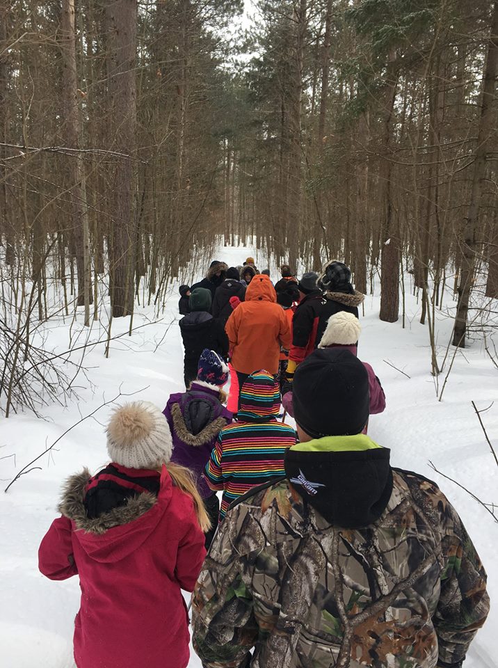 group of adults and children walking the forest path in the winter